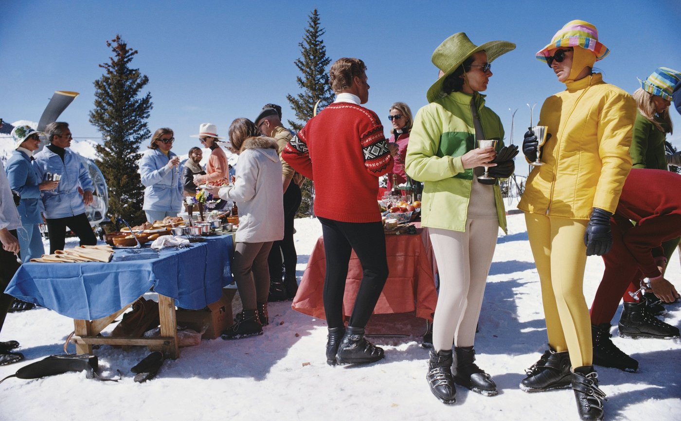 Two women in vibrant skiwear stand among the crowd of partygoers at Snowmass Village. PHOTO BY SLIM AARONS/STRINGER/COURTESY OF GETTY