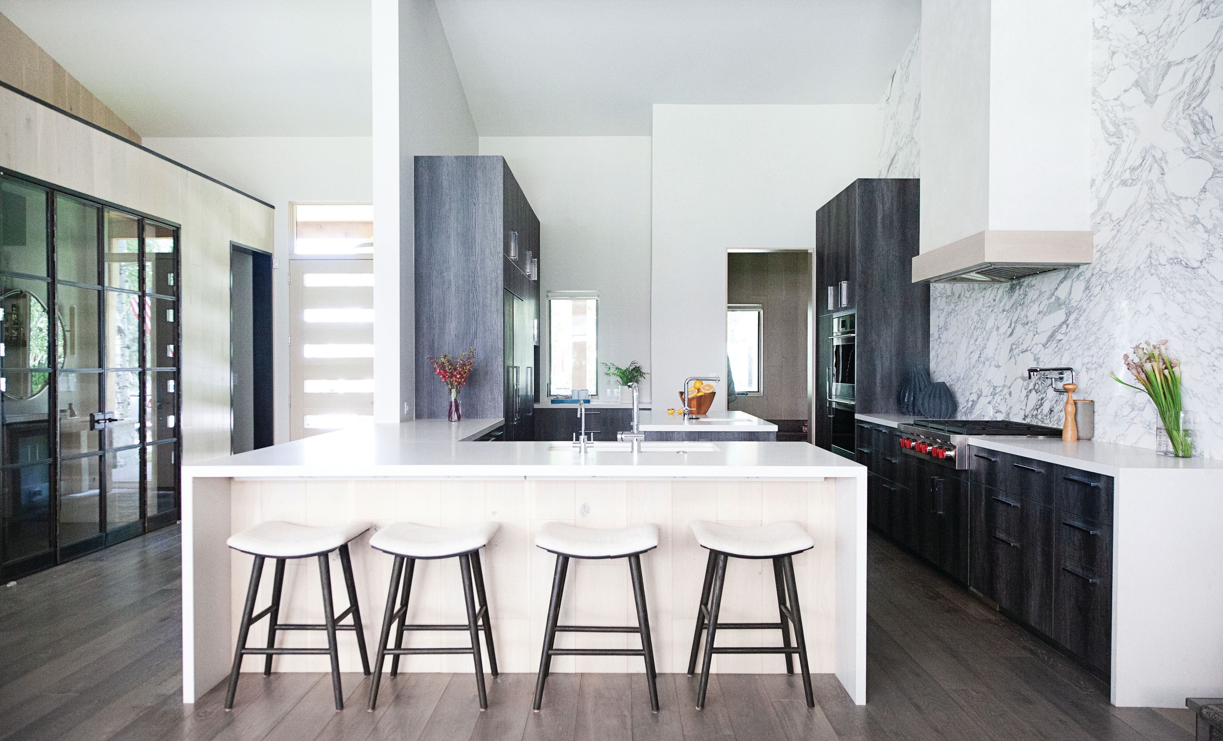 Setting the tone for the interiors, the primarily white kitchen is accented with Calacatta marble, a Caeserstone island and Canyon Charcoal detailing. Counter stools are by Four Hands. PHOTOGRAPHED BY BROOKE CASILLAS
